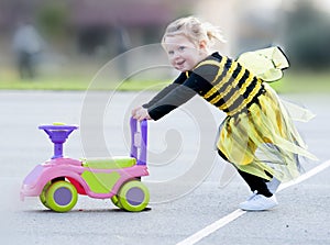 Happy blond little girl in bee costume pushing toy