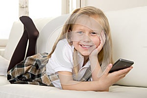 Happy blond little girl on home sofa using internet app on mobile phone