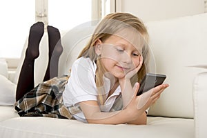 Happy blond little girl on home sofa using internet app on mobile phone