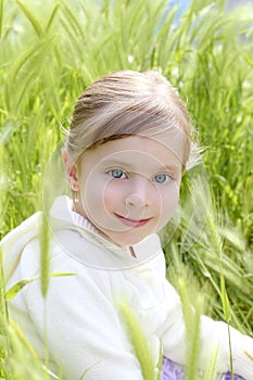 Happy blond little girl sit on green spikes meadow