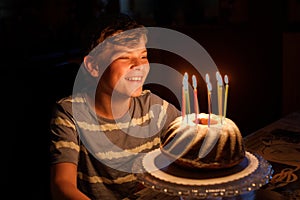 Happy blond little kid boy celebrating his birthday. Child blowing candles on homemade baked cake, indoor. Birthday