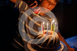 Happy blond little kid boy celebrating his birthday. Child blowing candles on homemade baked cake, indoor. Birthday