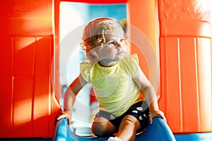 Happy blond little toddler girl having fun and sliding on indoor playground at daycare or nursery. Positive funny baby