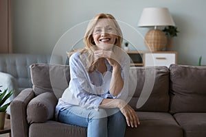 Happy blond middle aged attractive woman sitting on comfortable couch