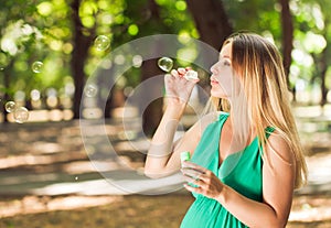 Happy blond pregnant woman blow bubbles in park