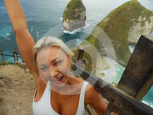 Happy blond tourist woman feeling free on the stunning view of beautiful sea cliff beach at viewpoint enjoying exotic Summer