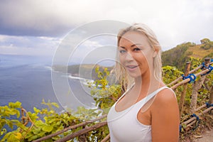 Happy blond tourist woman feeling free on the stunning view of beautiful sea cliff beach at viewpoint enjoying exotic Summer