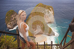 Happy blond tourist woman feeling free on the stunning view of beautiful sea cliff beach at viewpoint enjoying exotic Summer