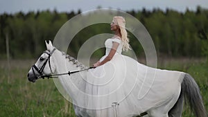 happy blonde bride is riding horse over meadow at summer, beautiful woman on horseback