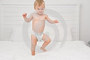 Happy blonde caucasian baby girl about 1 year old laughing jumping on white bedlinen in bedroom at home.Kid having fun