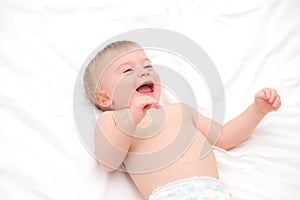 Happy blonde caucasian baby girl about 1 year old laughing lying on back on white bedlinen.Infant having fun before