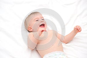 Happy blonde caucasian baby girl about 1 year old laughing lying on back on white bedlinen.Infant having fun before photo