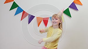 Happy Blonde caucasian kid girl in birthday hat child dancing and having fun.