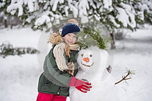 Happy blonde cute child girl plaing with a snowman