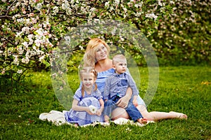 A happy blonde family, a chubby mom and two kids a boy and a girl in a blooming spring apple orchard on a spring picnic