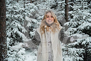 Happy blonde girl with blue eyes throws snow flakes from her hands. Beautiful portrait with bokeh in the winter forest.