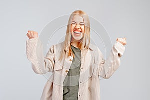 Happy blonde girl rejoicing her success and victory clenching her fists with joy. Lucky young woman being happy to achieve her aim