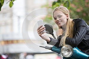 Happy blonde girl on scooter using cell phone