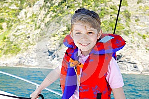 Happy blonde kid boy enjoying sailing boat trip. Family vacations on ocean or sea on sunny day. Healthy beautiful school