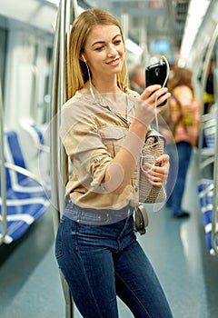 Happy blonde listening to music on headphones in a subway car