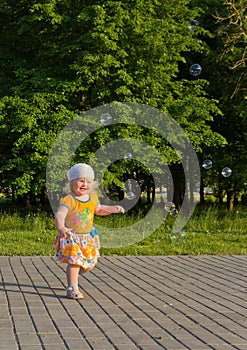 Happy blonde little girl in the summer having fun with soap bubbles outdoors