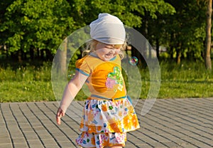Happy blonde little girl in the summer having fun with soap bubbles outdoors