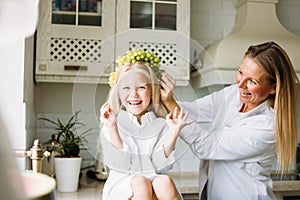 Happy blonde long hair mom and daughter having fun with grapes in kitchen, healthy family lifestyle