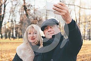 Happy blonde mature woman and beautiful middle-aged brunette take selfie on mobile phone. Loving couple of 45-50 years old walks