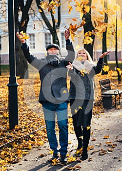 Happy blonde mature woman and handsome middle-aged brunette man walk in park and toss leaves. A loving couple of 45-50 years old