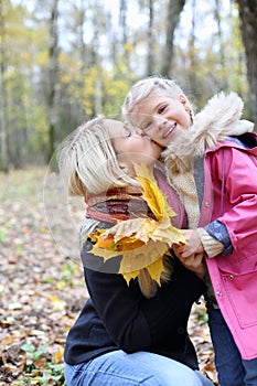 Happy blonde mother kisses her daughter with maple leaflets