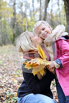 Happy blonde mother kisses her daughter with maple leaflets photo