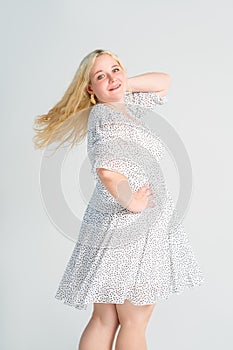 Happy blonde plus size model in polka dot dress, fat woman on gray background, body positive concept