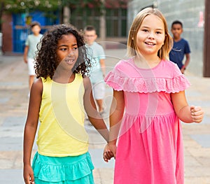 Happy blonde preteen girl walking with african american girl playmate