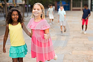 Happy blonde preteen girl walking with african american girl playmate photo