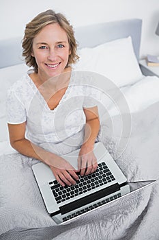 Happy blonde woman in bed using her laptop