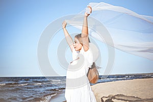 Happy blonde woman is catching clouds and wind with her arms on the ocean beach