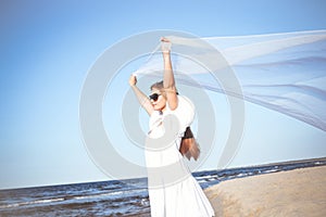 Happy blonde woman is catching clouds and wind with her arms on the ocean beach