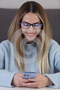 Happy blonde woman in glasses typing a message in modern smart phone app. Closeup portrait of young adult female using mobile