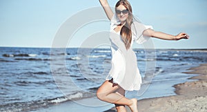 Happy blonde woman having fun on the ocean beach in a white dress and sunglasses