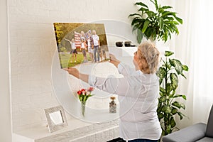 A happy blonde woman is holding a large wall canvas portrait of her family with young children.
