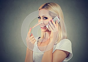 Happy blonde woman with long nose talking on mobile phone telling lies. Liar concept.