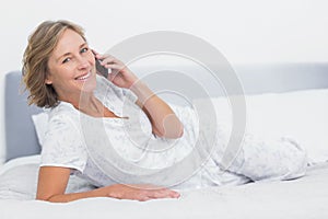 Happy blonde woman lying on bed making a phone call