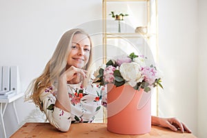 Happy blonde woman in a modern office with flowers in a hat box. Bouquet of peonies.