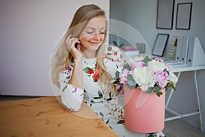 Happy blonde woman in a modern office with flowers in a hat box. Bouquet of peonies.