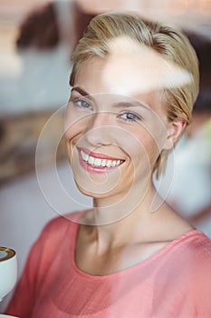 Happy blonde woman smiling at camera and holding a cup of coffee