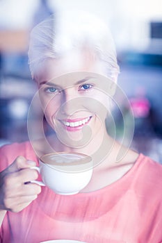 Happy blonde woman smiling at camera and holding a cup of coffee