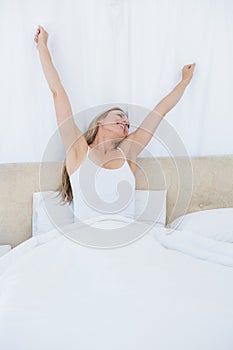 Happy blonde woman stretching in bed