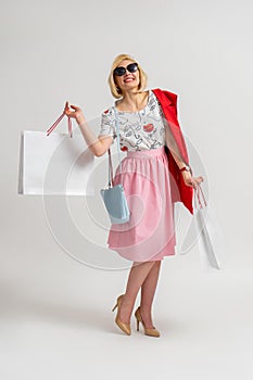 Happy blonde woman in sunglasses holding shopping bags in her hands and rejoices