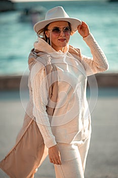 Happy blonde woman in a white suit and hat posing at the camera against the backdrop of the sea