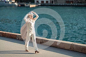 Happy blonde woman in a white suit and hat posing at the camera against the backdrop of the sea